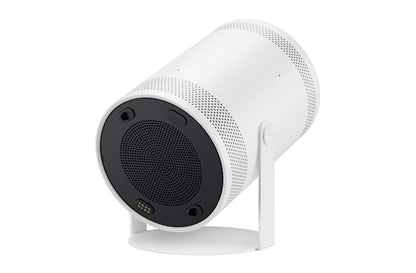 A white cylindrical portable projector with a black circular front grille and a white stand, shown on a solid white background.