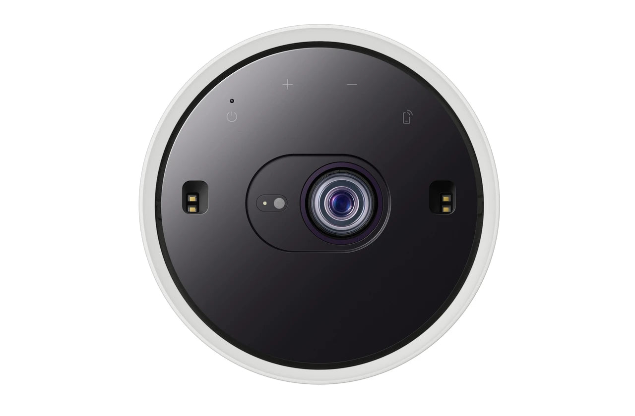 A top-down view of a circular smart home cenima projector with a black face, white outer rim, and a blue-tinted lens, shown on a solid white background.